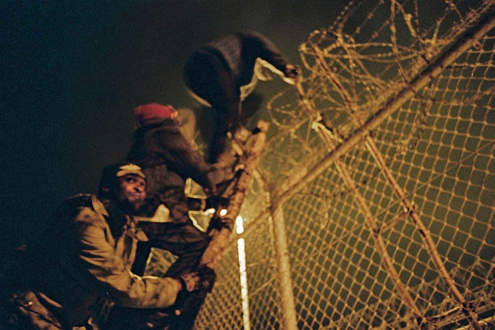 Men look out for police as they climb the fence separating Morocco and Melilla, a coastal Spanish town.