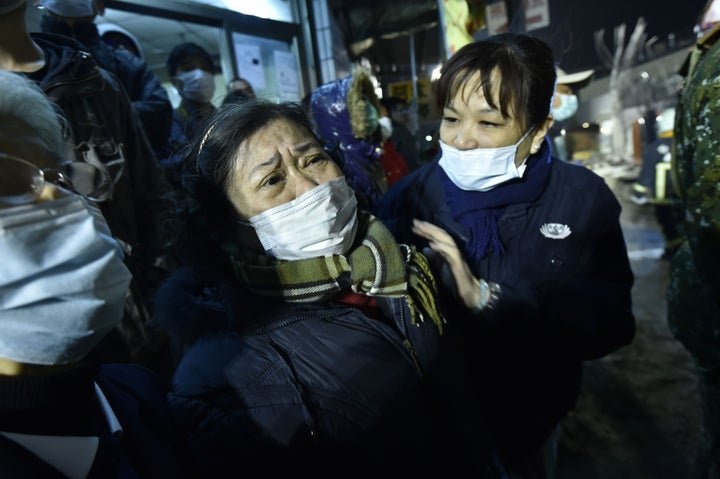 A woman (C) is comforted as rescue personnel continue work at the site of a collapsed building in the southern Taiwanese city of Tainan on February 6, 2016 following a strong 6.4-magnitude earthquake.