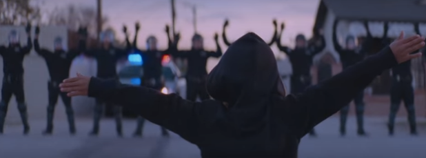 In another scene from the video, a young black boy in a black hoodie holds his arms out wide before a line of officers with their hands raised.