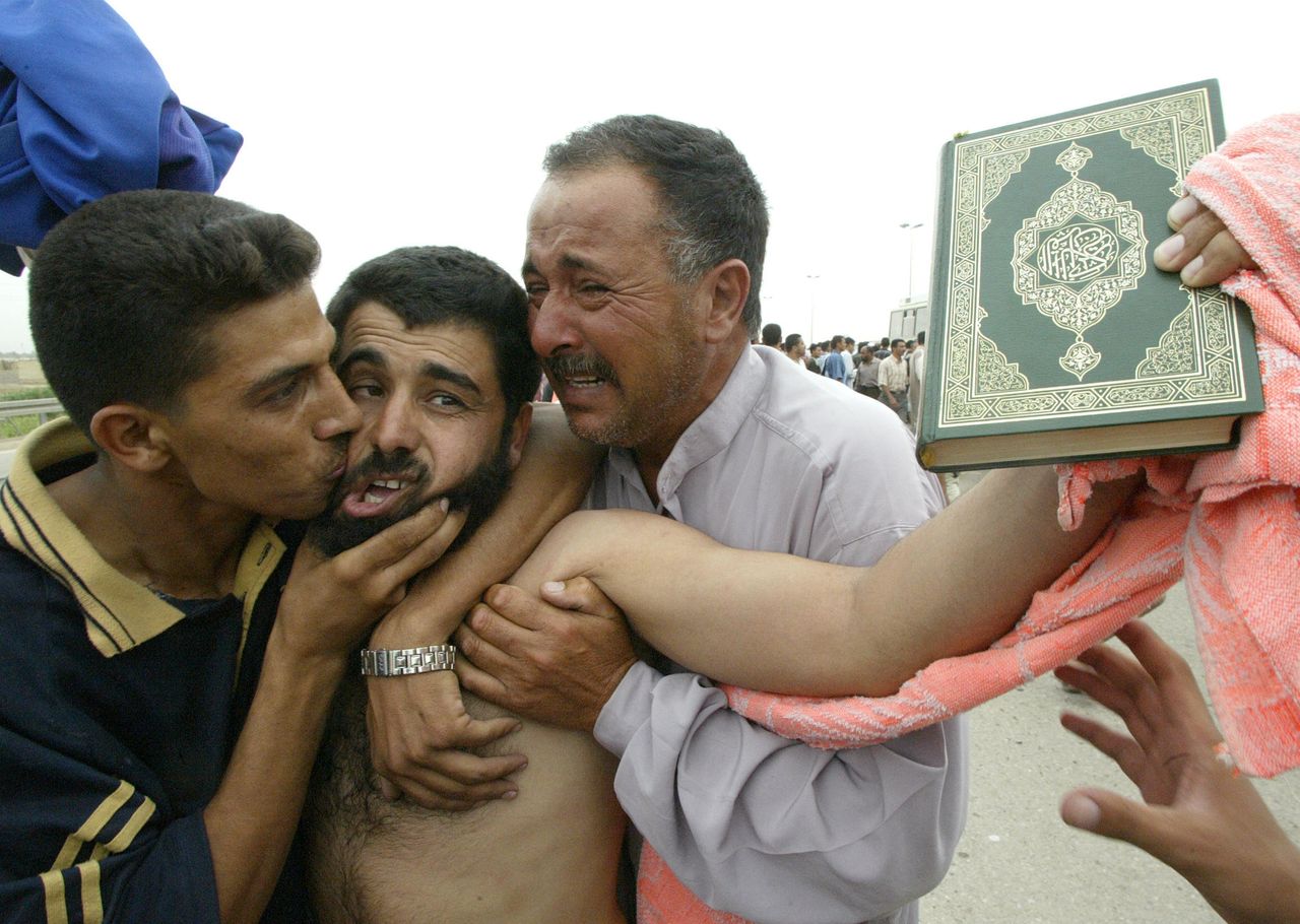 A freed prisoner holding up the Muslim holy Koran is hugged and kissed by family members after being released from the Abu Ghraib prison, west of Baghdad, 28 May 2004. 