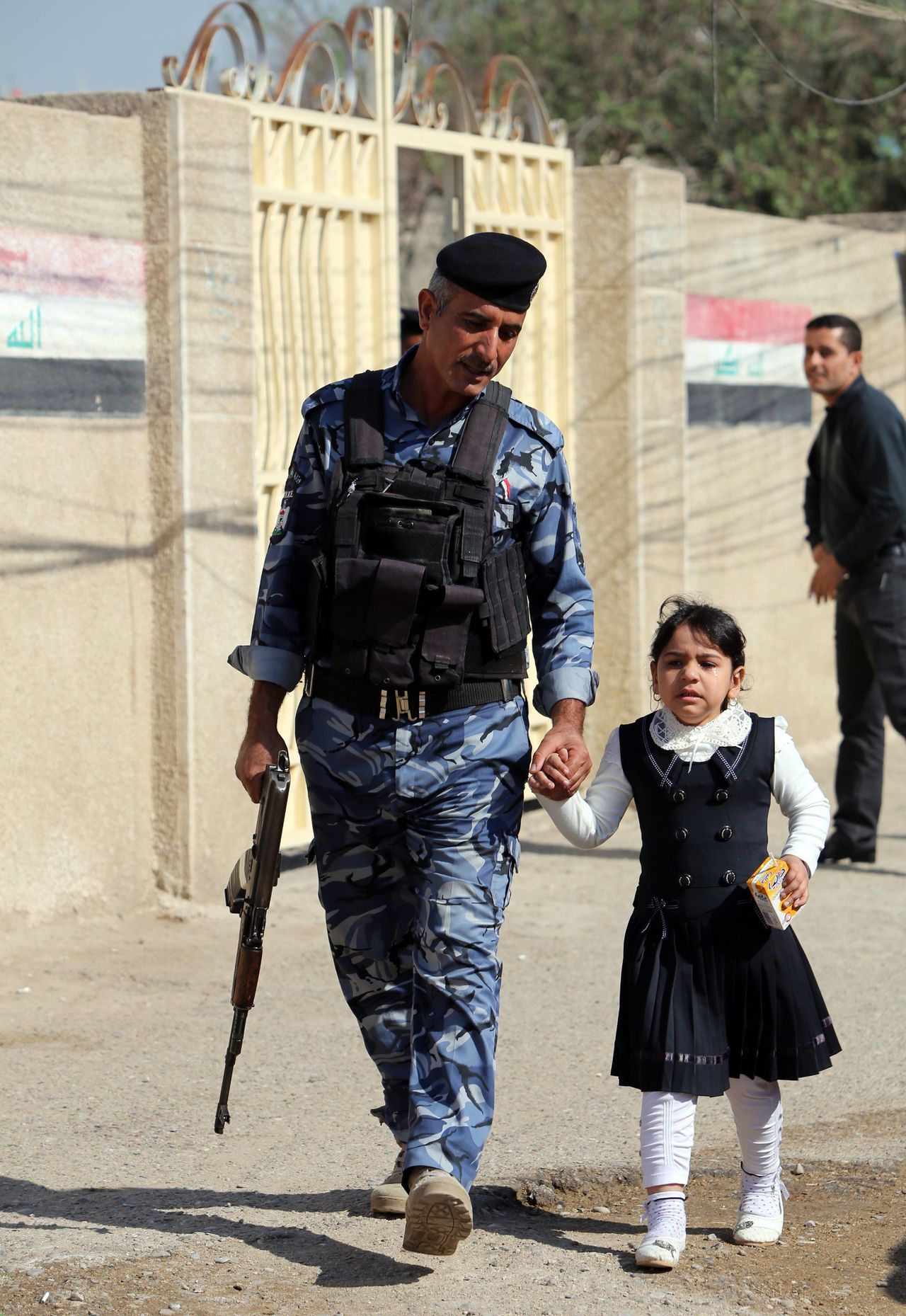 An Iraqi policeman holds a young girl’s hand near the entrance to a school on the first day of the new semester in Baghdad on October 22, 2014. 