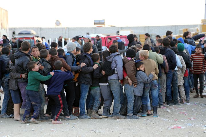 Syrians, who fled bombing in Aleppo, wait in line to get food at a tent city on the Turkish-Syrian border.