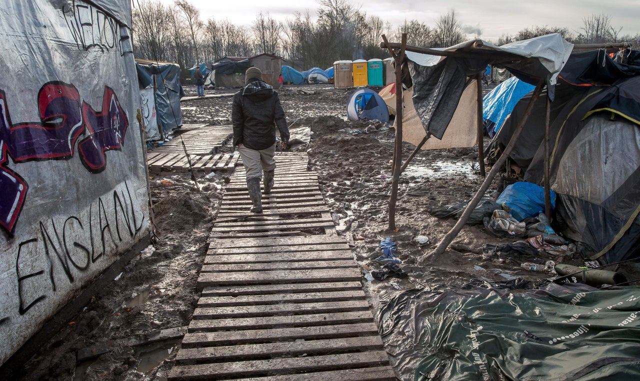 A man walks among tents and shelters in Grande-Synthe, next to a sign saying "We Love England." Most of the camp's inhabitants hope to cross the English Channel into the United Kingdom, where many have relatives and jobs.