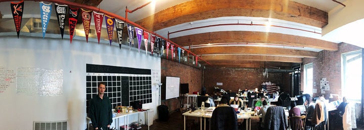 Jack Rivlin, co-founder of The Tab, at left, stands in their Brooklyn office below pennants representing the campuses where they have writers.