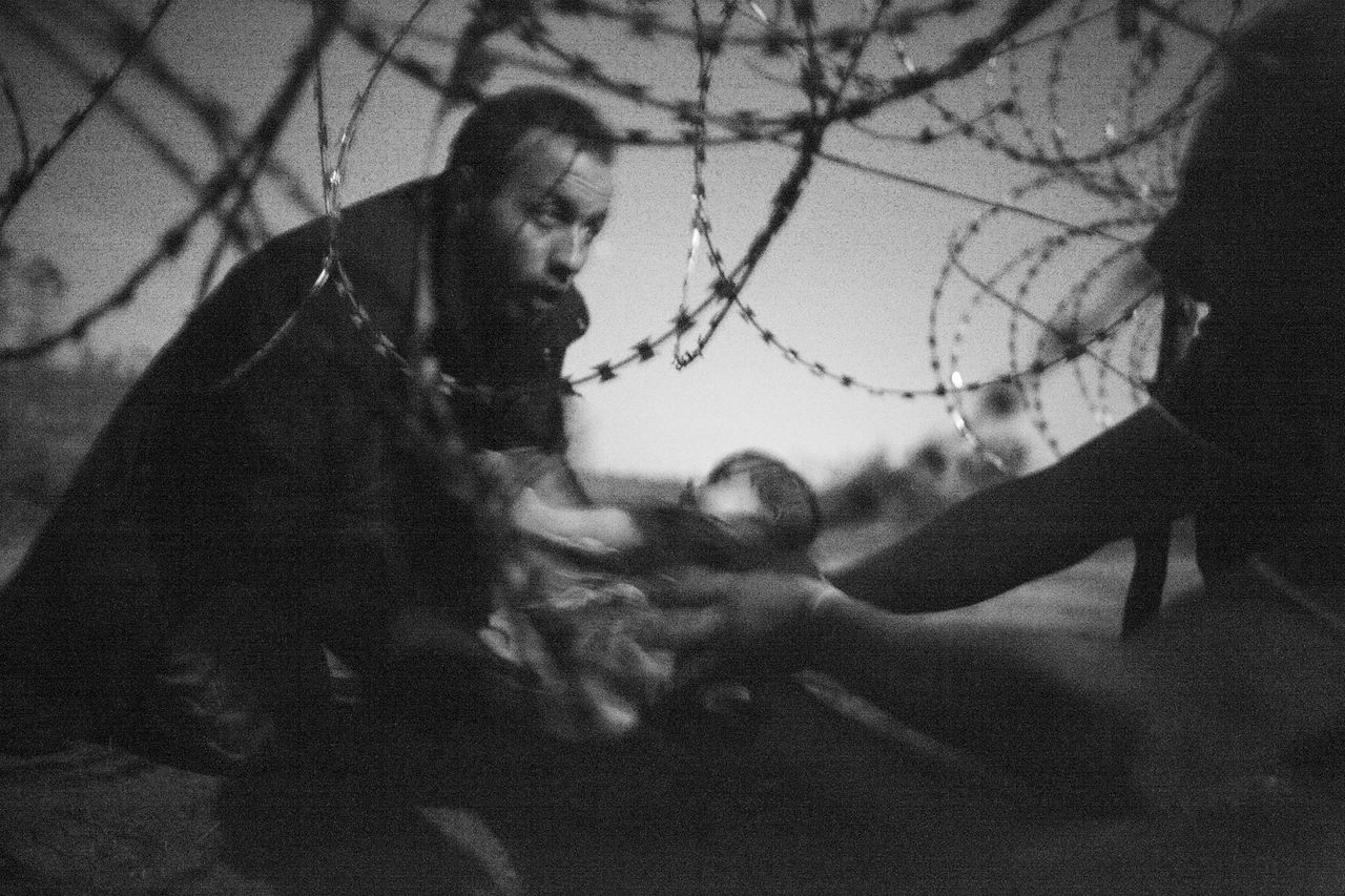 A man passes a baby through the fence at the Hungarian-Serbian border in Röszke, Hungary, 28 Aug. 2015.