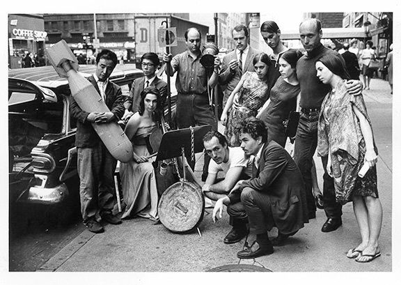 Peter Moore. Publicity photograph for 3rd Annual New York Avant Garde Festival, August 26, 1965. Left to right: Nam June Paik, Charlotte Moorman, Takehisa Kosugi, Gary Harris, Dick Higgins, Judith Kuemmerle, Kenneth King, Meredith Monk, Al Kurchin, Phoebe Neville. In front, kneeling, Philip Corner and James Tenney. Photograph © Barbara Moore/Licensed by VAGA, NY.