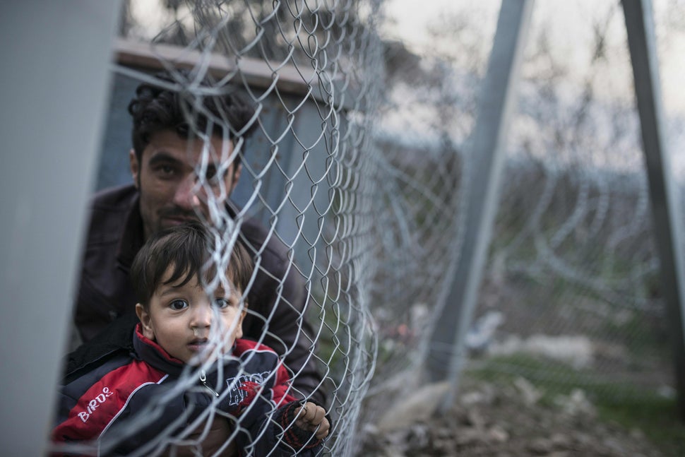 A man and a boy on the Greek side of the border look through a fence into Macedonia, which closed its borders to Af