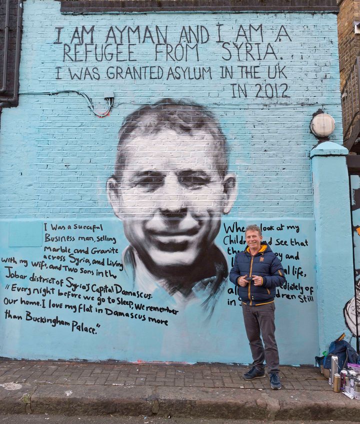 Ayman Hirh stands in front of the striking mural that he created with London street artist PANG.