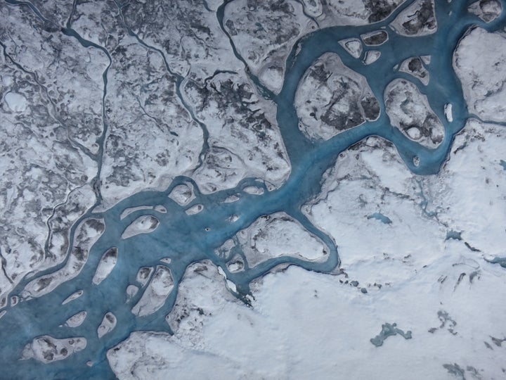 An aerial image of Greenland shows rivers of meltwater and areas of dark ice. Greenland's surface is absorbing more solar rad