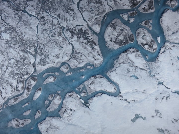 An aerial image of Greenland shows rivers of meltwater and areas of dark ice. Greenland's surface is absorbing more solar radiation as melting increases grain size and brings old impurities to the surface.