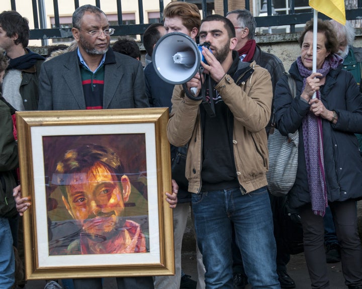 A man holds a framed picture of Giulio Regeni and beside him a man speaks using a megaphone during a protest in front of
