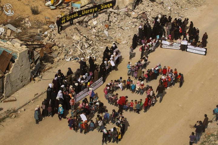 Dozens of people in Daraya, a besieged Syrian town, appealed for international help through a massive SOS sign and placards calling on world leaders.