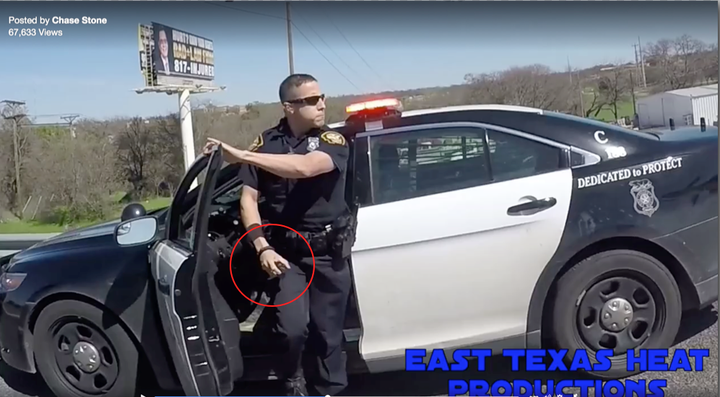 A man wearing a police uniform is seen exiting a marked police cruiser with what appears to be a canister in his hand.