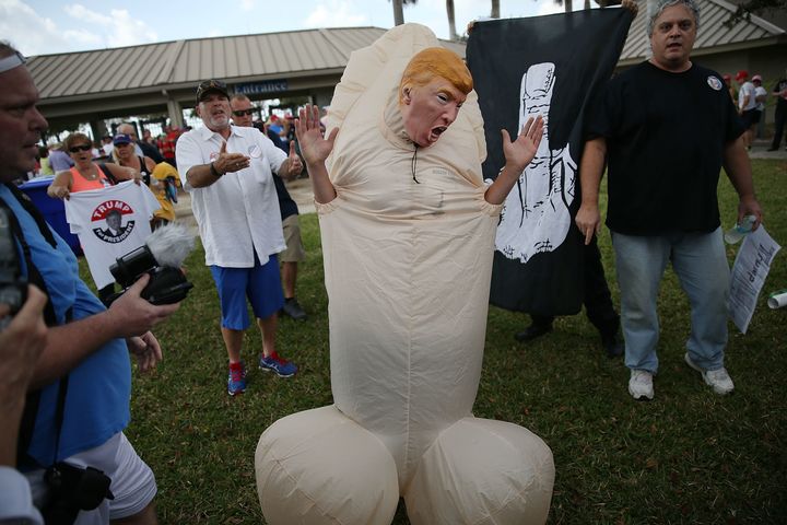 A person dressed as a phallic symbol and wearing a Donald Trump mask is seen as people wait to enter a rally for Republican presidential candidate Donald Trump at the Sunset Cove Amphitheater on March 13, 2016 in Boca Raton, Florida. Mr. Trump continues to campaign before the March 15th Florida primary. (Photo by