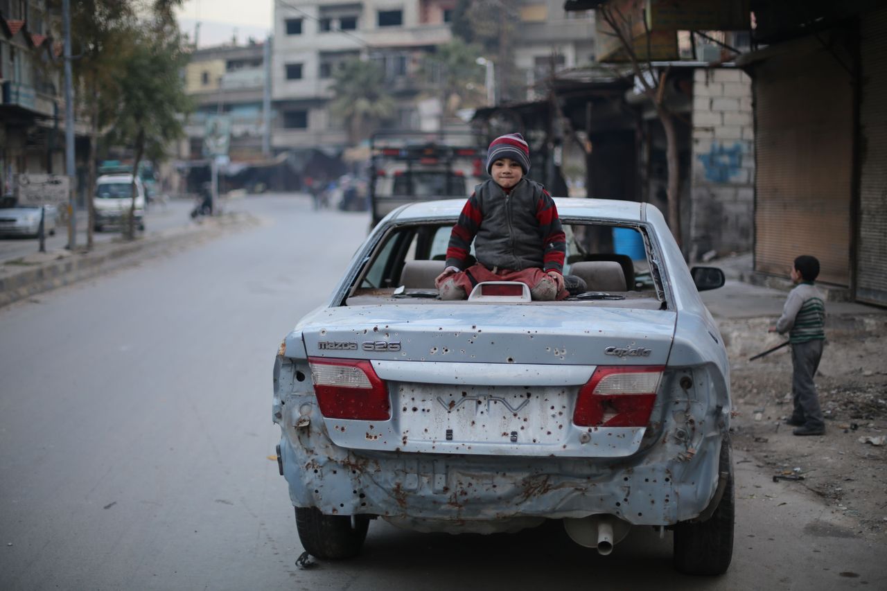 A child sits on a car destroyed by an explosion in Ghouta, Syria.