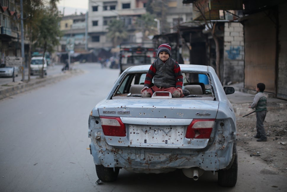 A child sits on a car destroyed by an explosion in Ghouta, Syria.