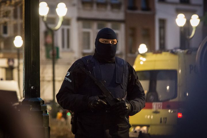 Belgian authorities identified the gunman killed in a raid targeting suspects in the Paris attacks as a 35-year-old Algerian. Police also detained two other suspects. A police officer takes post around the raid area in Brussels.