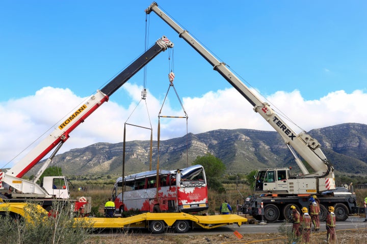 Emergency personnel look on as two cranes hoist the bus onto a trailer