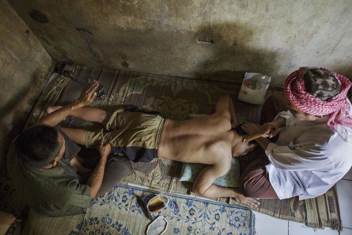 Haji Hamden, an Islamic faith healer, chants as his assistant Abdul slaps the leg of a shelter resident at Pengobatan Alternatif Nurul Azha, a traditional healing center, in West Java. Abdul also uses a hard implement to massage patients, causing extensive bruising, as part of the daily healing routine.