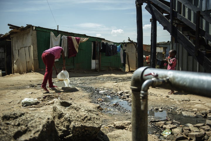A resident of the Zandspruit informal settlement in Johannesburg empties a bucket of watsed water into a polluted stream next