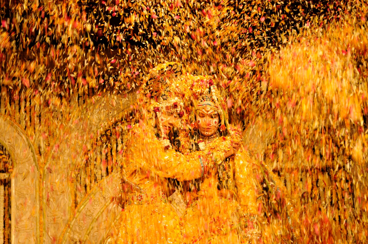 Indian artists dressed up as Hindu Lord Krishna and his consort Radha are showered with flower petals during Holi celebrations at Shri Chaitanya Prem Sansthan