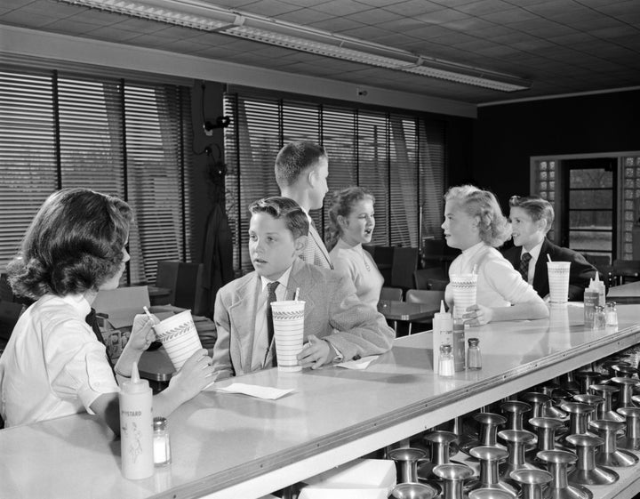 Teens sit at a soda fountain in the 1950s to drink milkshakes.