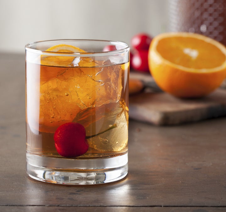 A classic old-fashioned cocktail with a cherry on a wooden table.