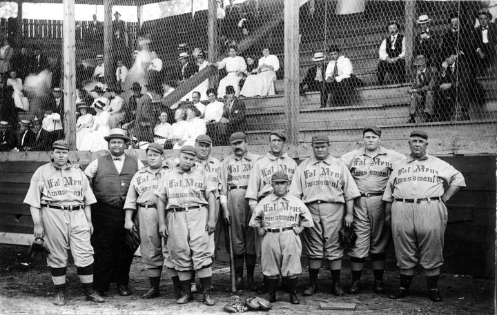 Players on The Fat Man's Baseball Association, wear jerseys written with "Fat Mens Amusement" across it and pose in their home ballpark (unknown location) in 1910.