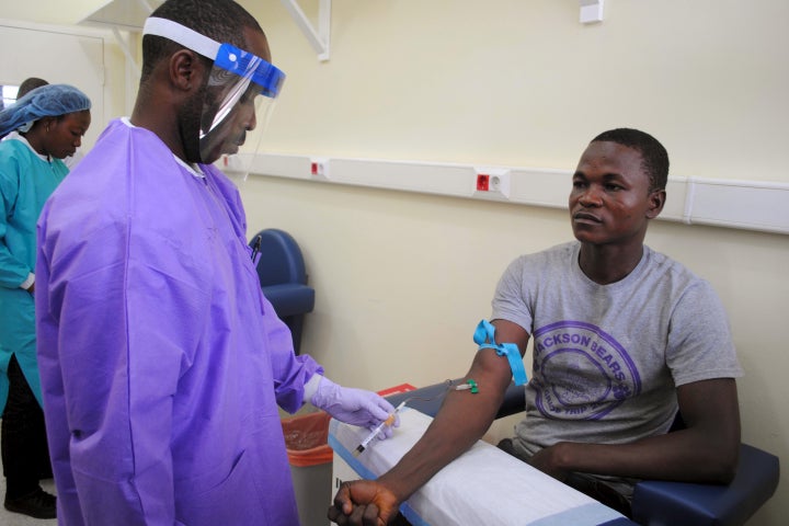 A healthcare worker takes a blood sample from an Ebola survivor as part of a study on the disease, in Monrovia, Liberia, June