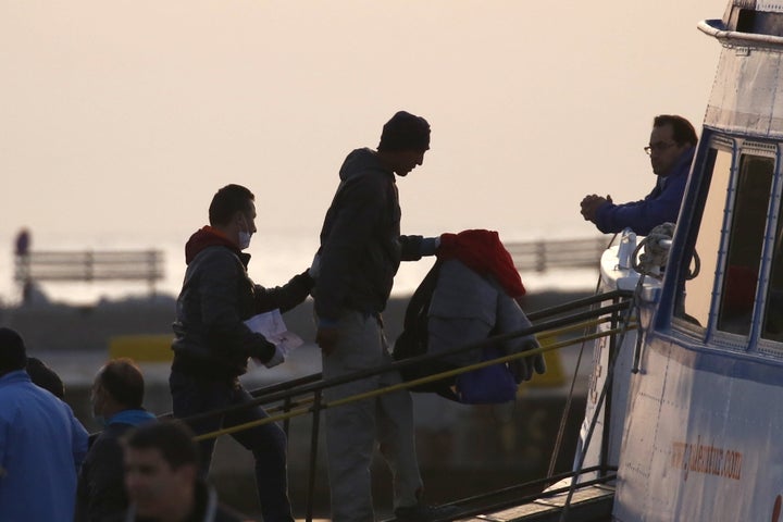 A Frontex officer escorts a migrant on board a passenger boat to Turkey, on the Greek island of Lesbos.