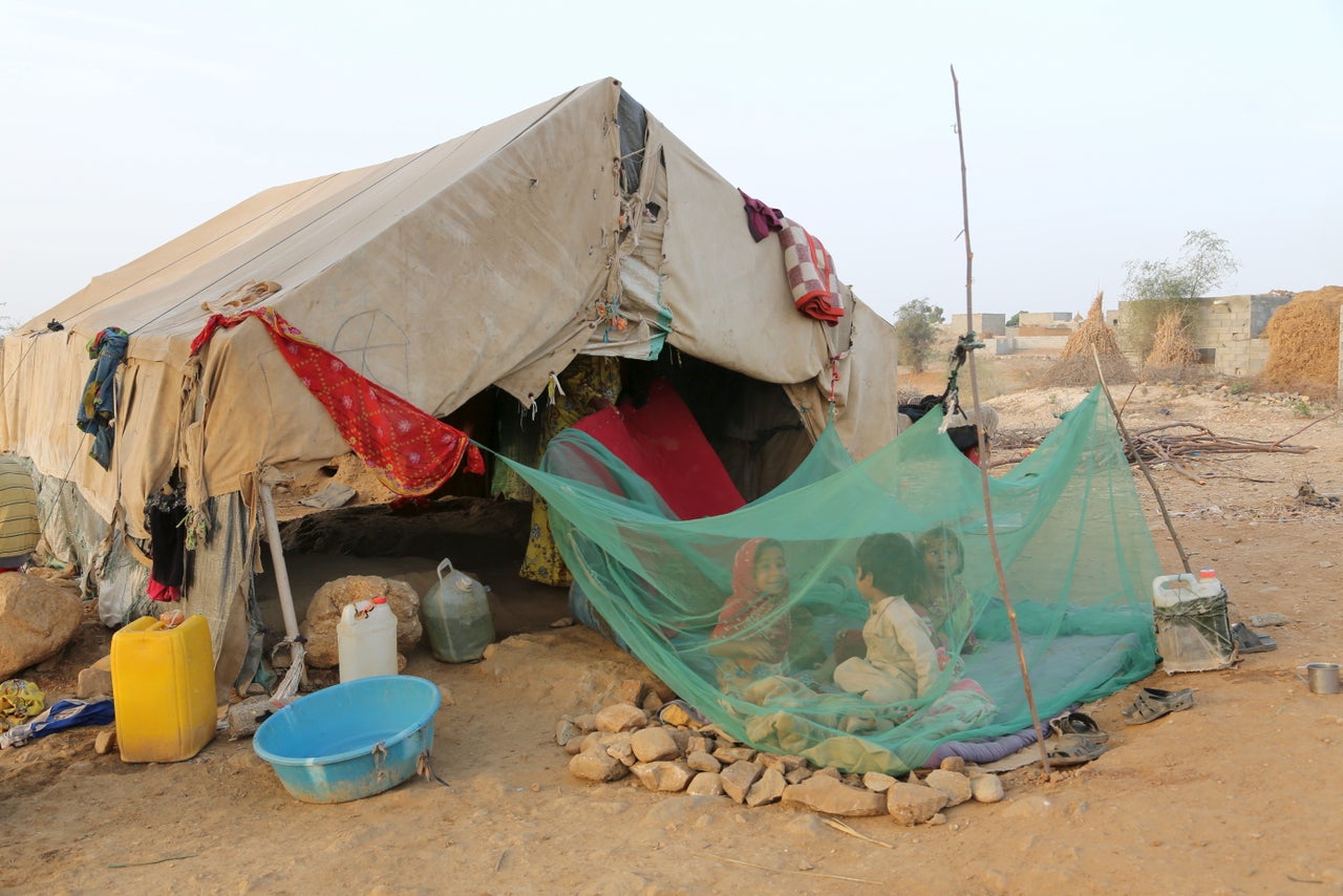 In the camp, medical treatment is hard to come by for both old and young. Children sit under a mosquito net outside their family's hut in the camp.