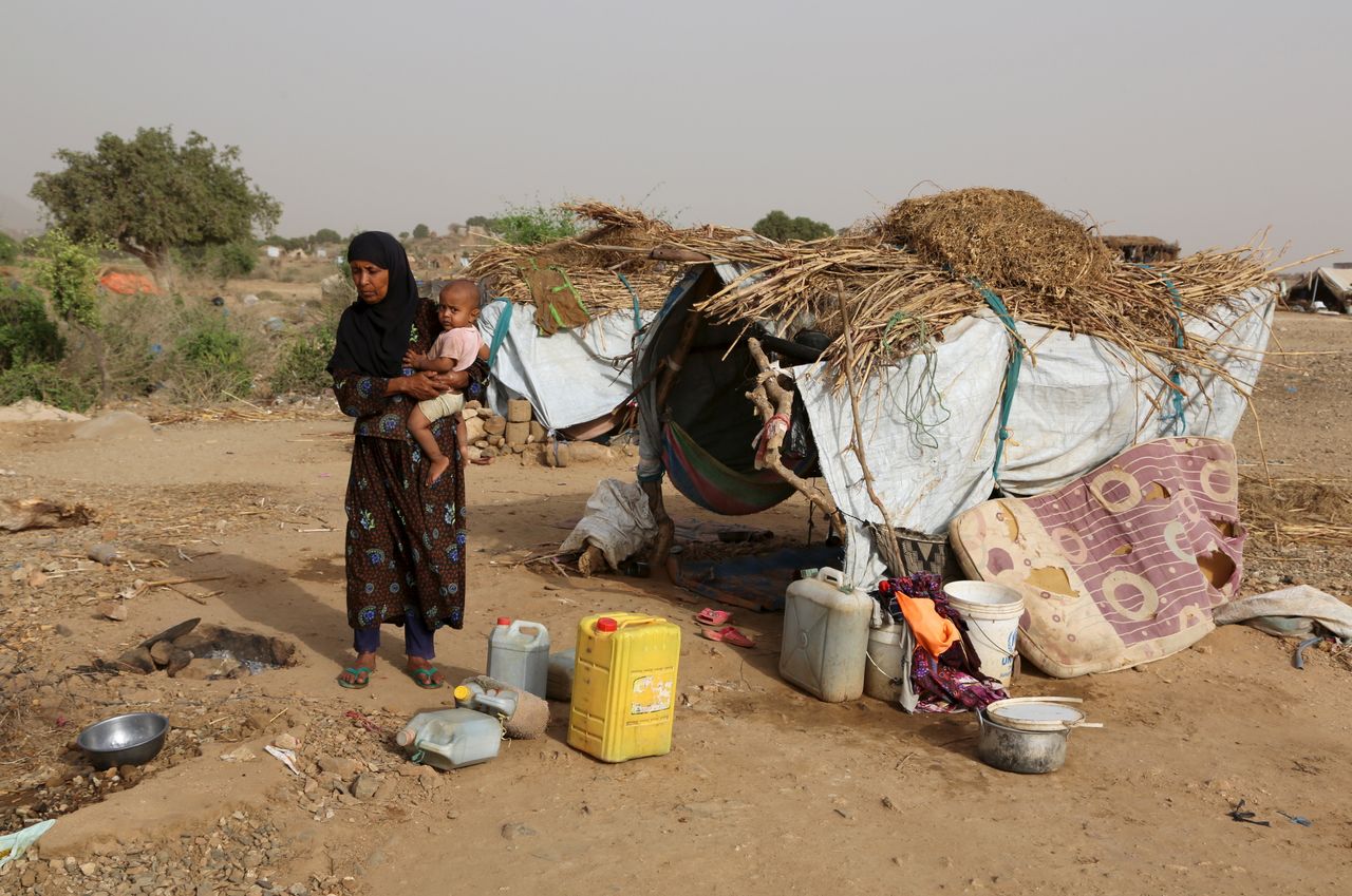 A woman carries a child at the Shawqaba camp. The residents of the camp live in poorly built huts that protect them neither from summer heat nor winter cold.