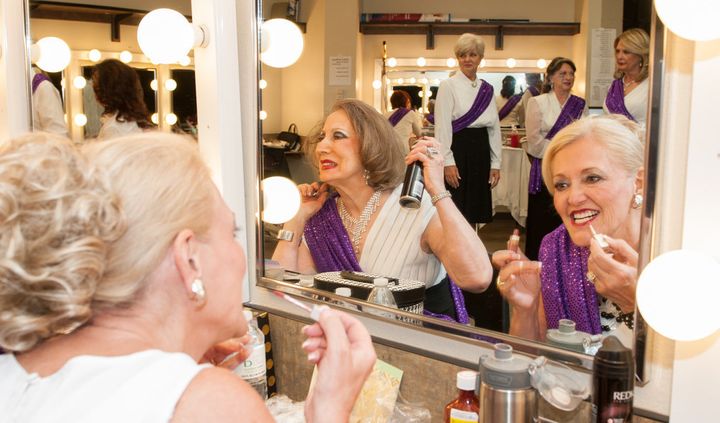 Two contestants work on their hair and makeup backstage. 