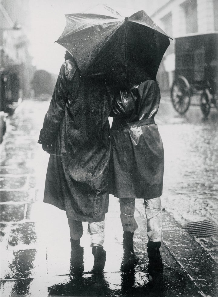 A couple stays dry during a 1930s storm wearing Mackintosh jackets around their backs and newsprint around their legs.