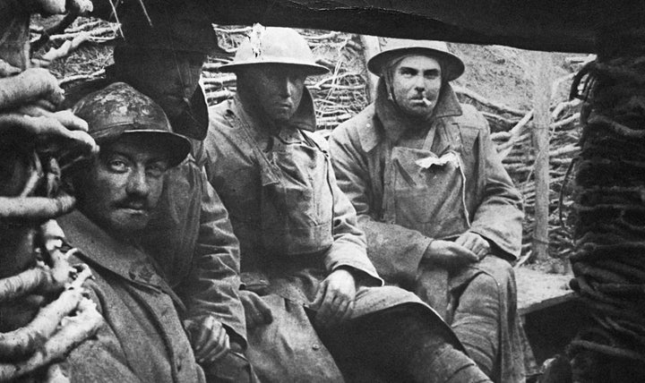 British soldiers hunker in a trench wearing trench coats during WWI in 1914.