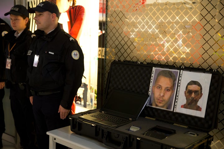 Police officers stand next to the wanted notice of Abrini (R) and Abdeslam, who was arrested on March 18 in Brussels, four days before the Brussels Attacks.