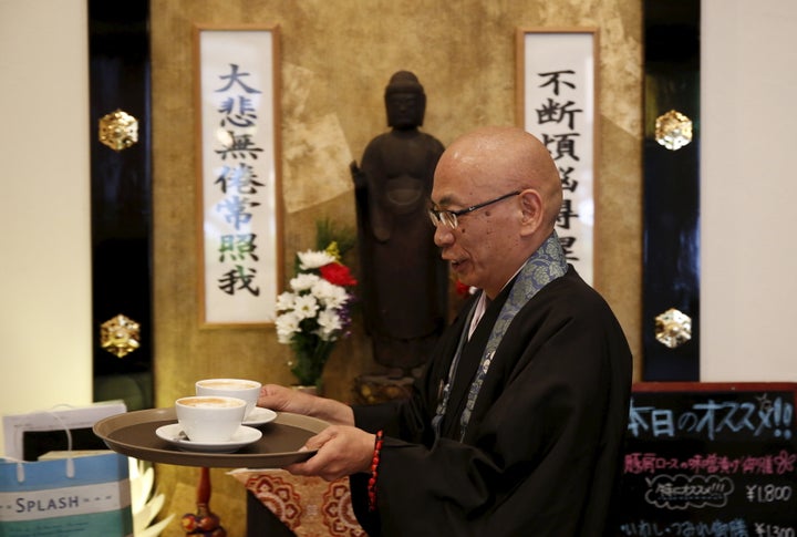 Shokyo Miura, a Buddhist monk and one of the on-site priests, carries cups of coffee past a statue of Buddha at Tera Cafe in Tokyo, Japan, April 1, 2016.