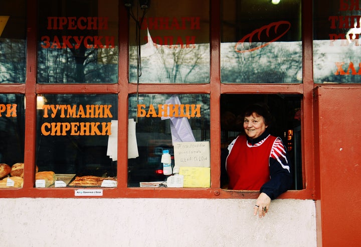 Shop-keeper at a small bakery in downtown Sofia, Bulgaria, inviting customers with a smile.