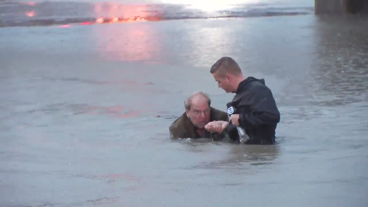 A local TV reporter is seen helping guide the driver out of the water and to higher ground.