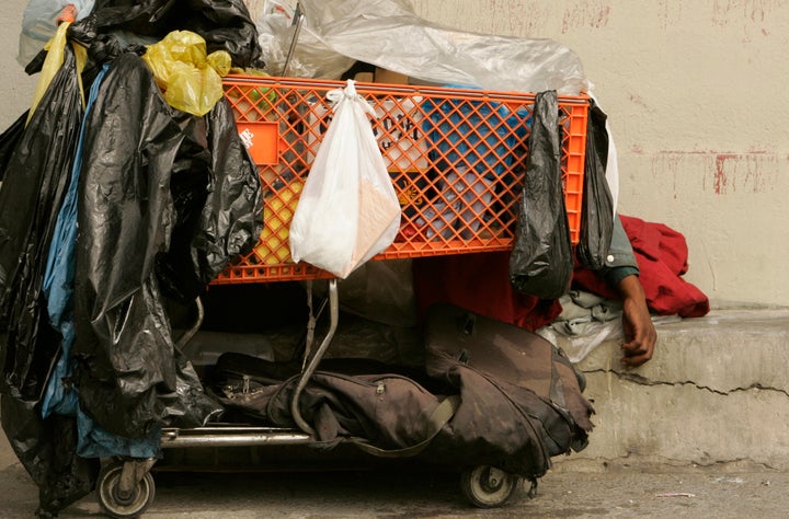 A homeless man sleeps behind his shopping cart on a sidewalk on downtown Los Angeles.