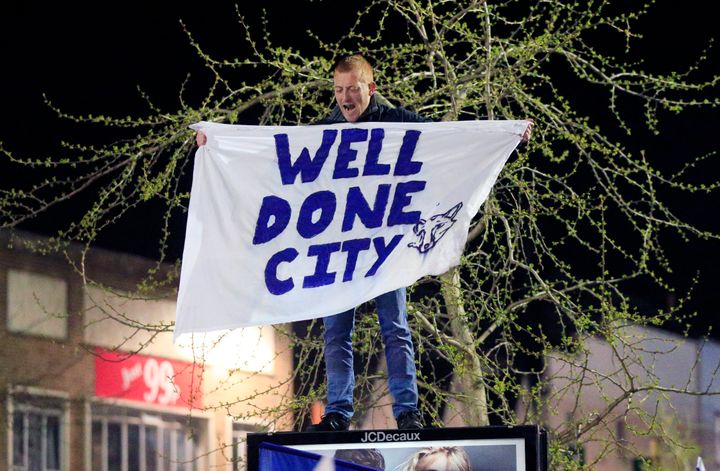 A Leicester City fan stands on top of an advertising board