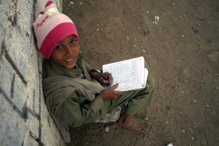 A Yemeni young boy poses as he writes in an exercise book sitting outside a minibus (unseen) turned into a mobile classroom o