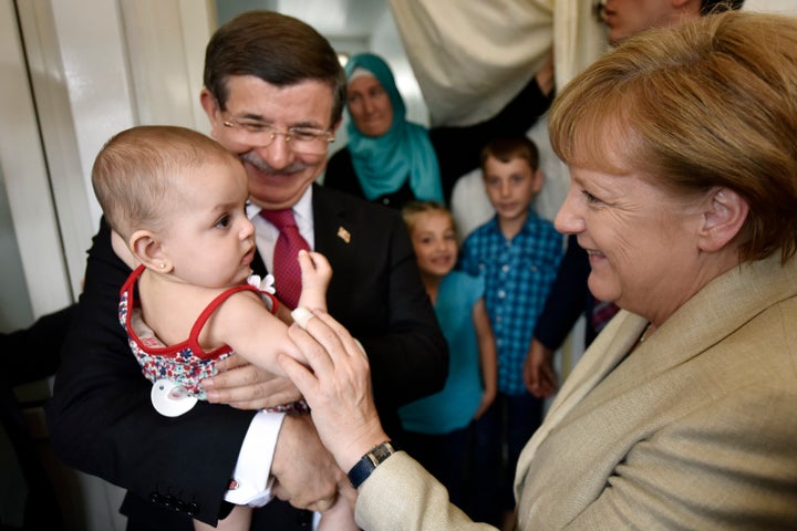 Turkish Prime Minister Ahmet Davutoglu and German Chancellor Angela Merkel pose with a child in a refugee camp on A