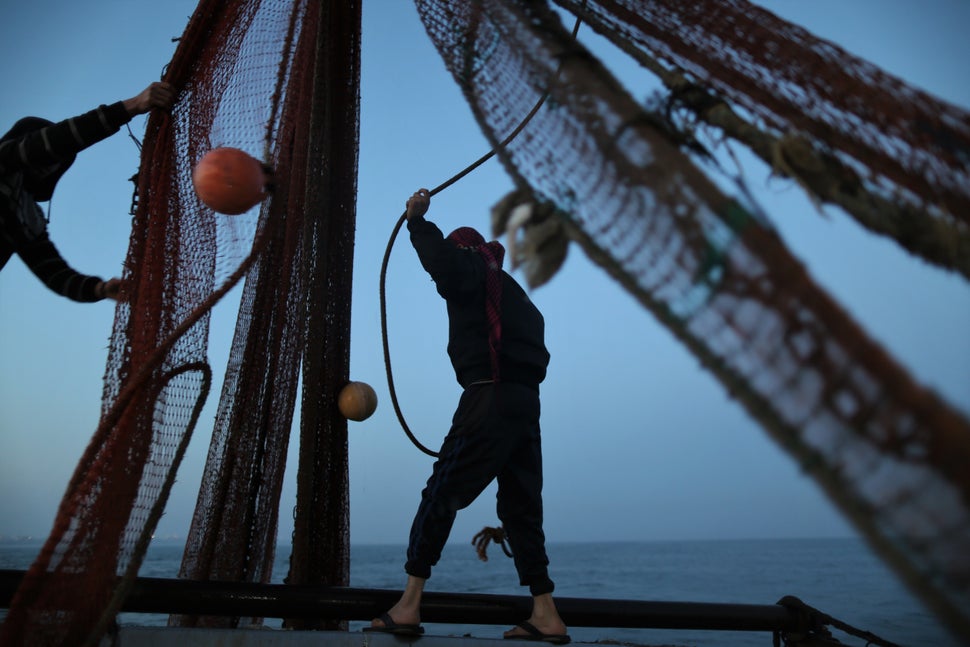 Palestinian fishermen organize their fishing net to make sure that nothing is stuck in it before they throw it back to the se