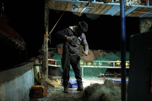 Mohammed Abu Owda collects useful materials from a broken fishing net they found in the Gaza sea.