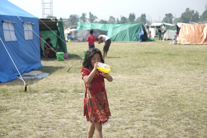 KATHMANDU, NEPAL - MAY 6: A girl drinks cold drinks as she walk to her camp at the earthquake victims camp site in Kathmandu, May 6, 2015. The number of the dead in the aftermath of Nepal's devastating earthquake has risen to 7,000 and more than 14,000 were injured according to figures from the Nepali police. (Photo by Sunil Pradhan/Anadolu Agency/Getty Images)