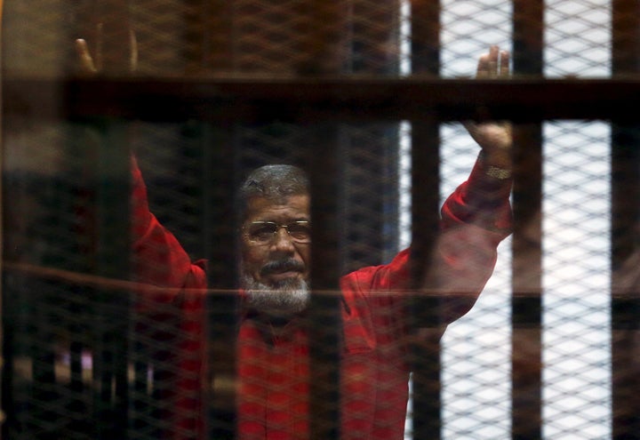 Deposed President Mohamed Mursi greets his lawyers and people from behind bars at a court wearing the red uniform of a prisoner sentenced to death, during his court appearance with Muslim Brotherhood members on the outskirts of Cairo, Egypt, June 21, 2015.