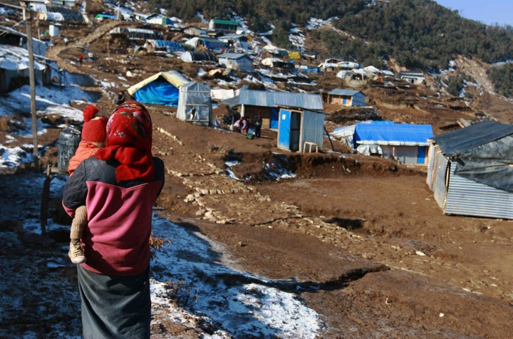 This photo taken on January 21, 2016 shows a Nepalese woman holding a child near temporary shelters in the Nepalese village of Laprak. Nine months after a massive earthquake hit Nepal, thousands of survivors are now fighting sub-zero temperatures in flimsy temporary shelters, awaiting government help to rebuild their homes. The threat of landslides had forced families in the remote village of Laprak, close to the quake's epicentre in western Nepal, to relocate to a site a thousand metres higher. AFP PHOTO / POOJA PANT / AFP / POOJA PANT (Photo credit should read POOJA PANT/AFP/Getty Images)