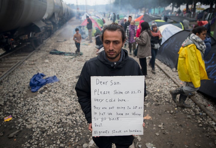 A man holds a handwritten sign near tents set up beside railway tracks at the northern Greek border point of Idomeni.