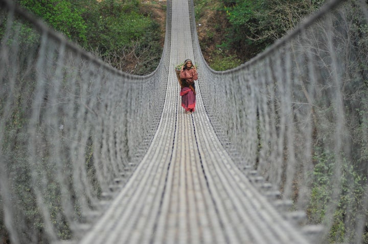 An old woman walks back home over a long bridge after collecting grass for domestic animals at Chhampi, Kathmandu, Nepal.